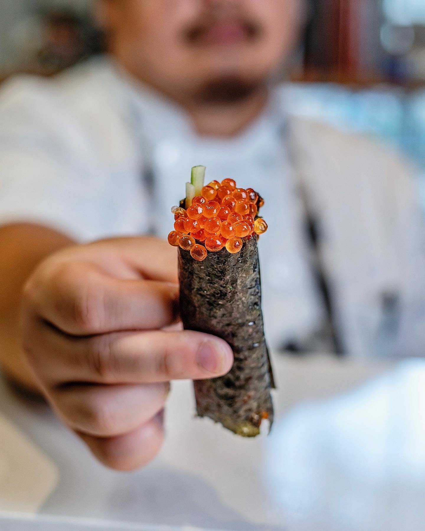 chef holding out a sushi roll with seaweed and fish eggs